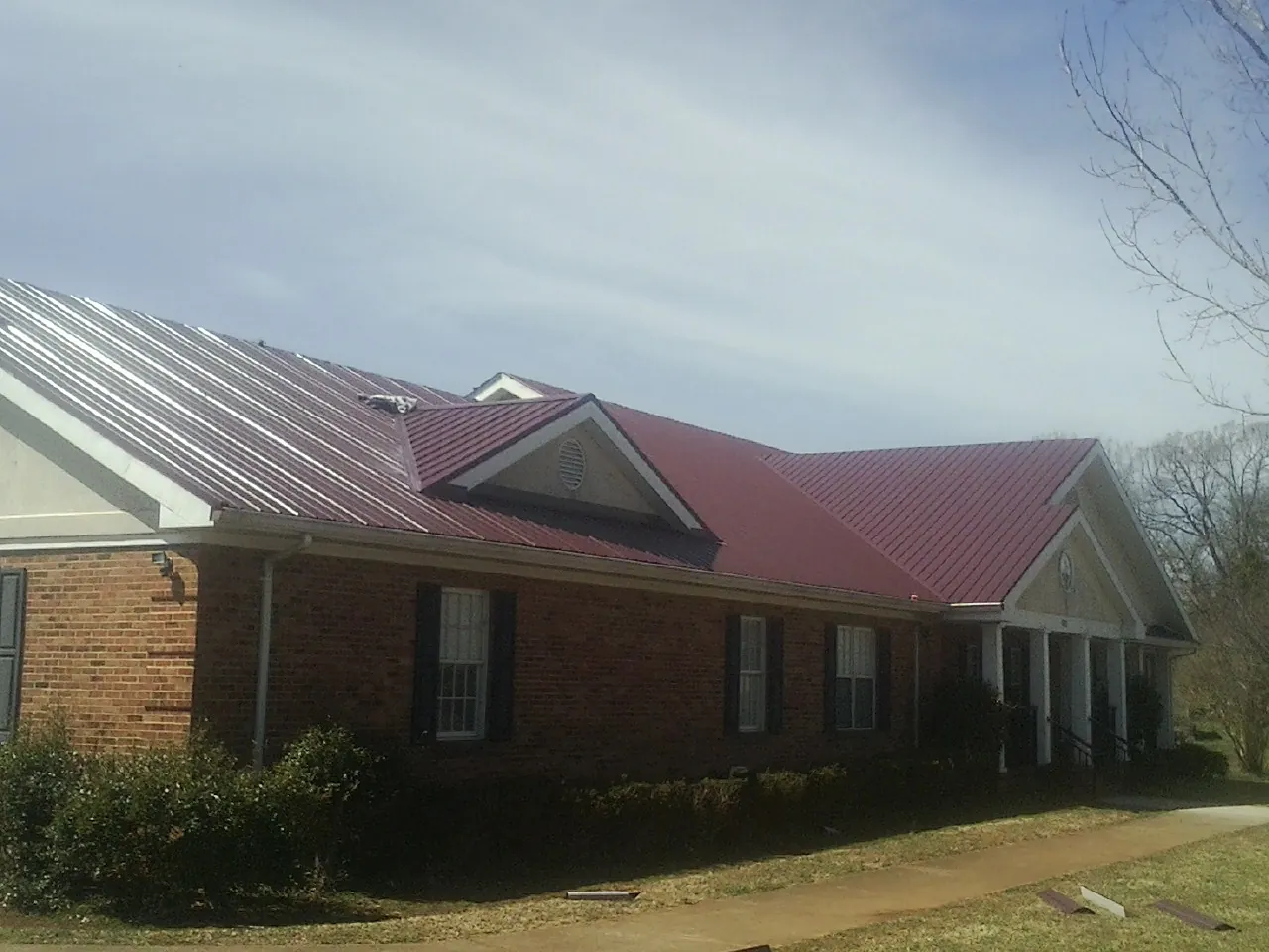 Red metal roof with gabled entries on a long brick building, from a Hail Damage Roof Repair job in Eastsound