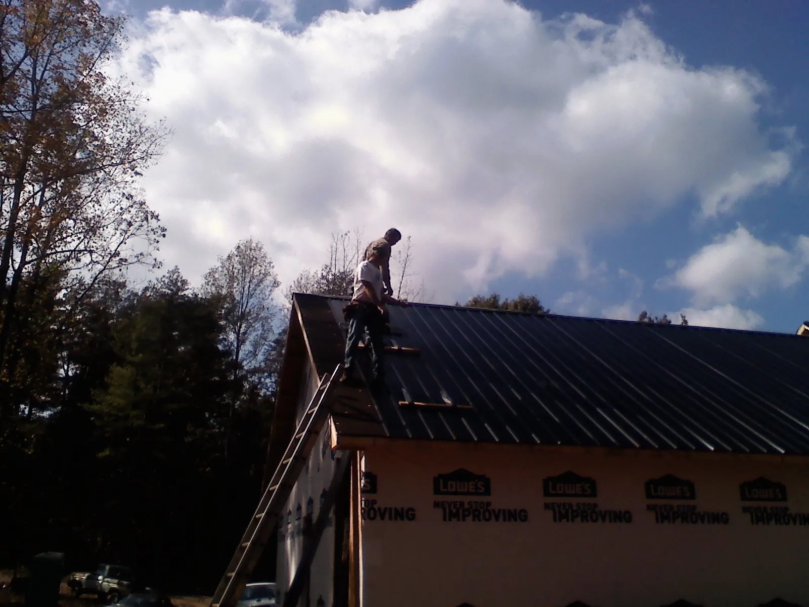 Roofer fastening dark metal panels high against a cloudy sky, from a Roof Inspection job in Eastsound